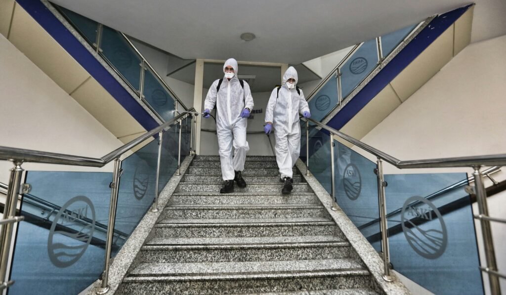 Two professional biohazard cleanup technicians in full white PPE protective suits descending stairs in a public building for decontamination