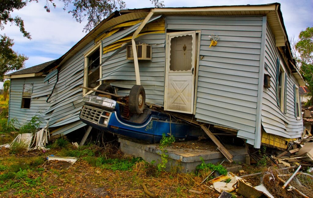 Severely storm damaged house with overturned vehicle underneath collapsed structure after natural disaster requiring emergency restoration